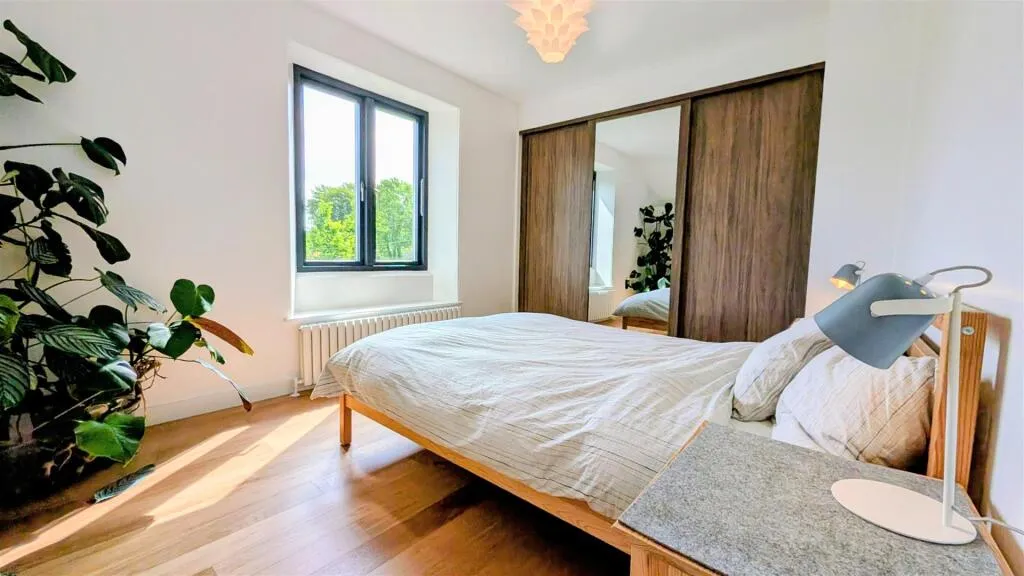 A bed room with a neatly made bed and a plant.