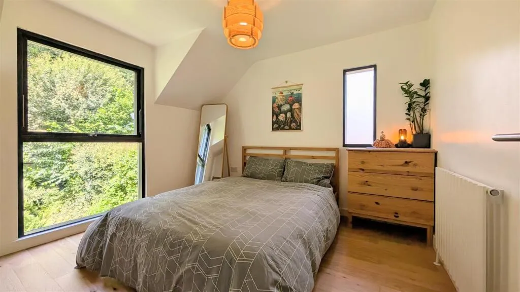 A bedroom with a bed, dresser, and large window.